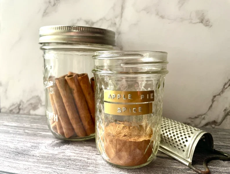 Jar of homemade apple pie spice mix with a rustic farmhouse feel, ideal for adding cozy fall flavor to seasonal recipes.