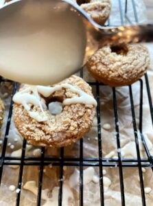 drizzling maple glaze on baked pumpkin donuts