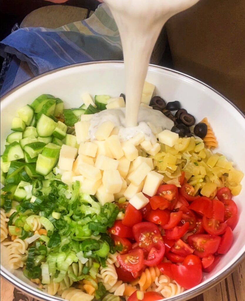 creamy Italian dressing being poured over pasta and veggies