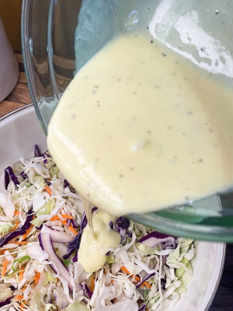 Pouring homemade creamy dressing over cabbage for coleslaw