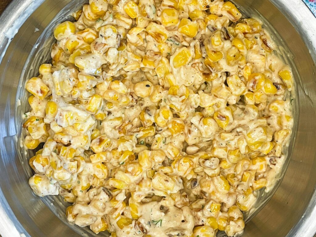 Skillet browned corn being mixed with creamy lime sauce for street corn chicken bowls.