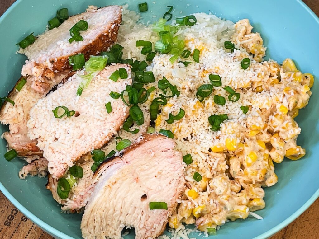 Street corn chicken bowl with rice, seasoned chicken, creamy corn, cotija cheese, lime, and herbs.