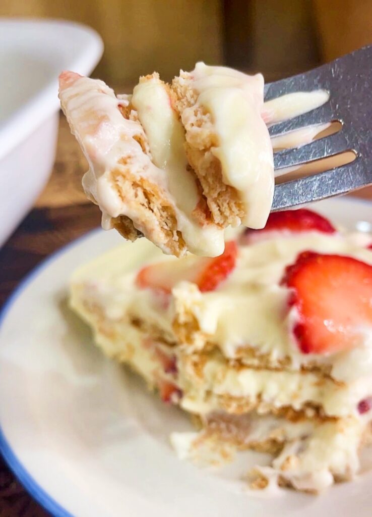 A bite  of strawberry icebox cake on a fork showing soft graham cracker layers and creamy vanilla filling.