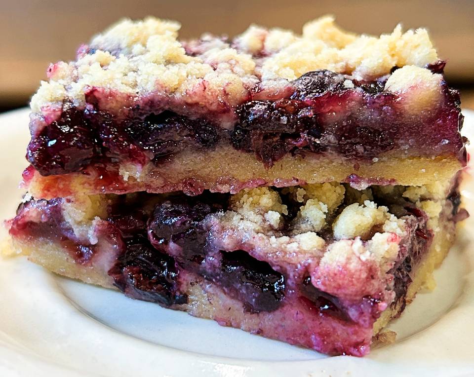 Blueberry crumble bars stacked on a plate with a buttery crumb topping and blueberry filling.