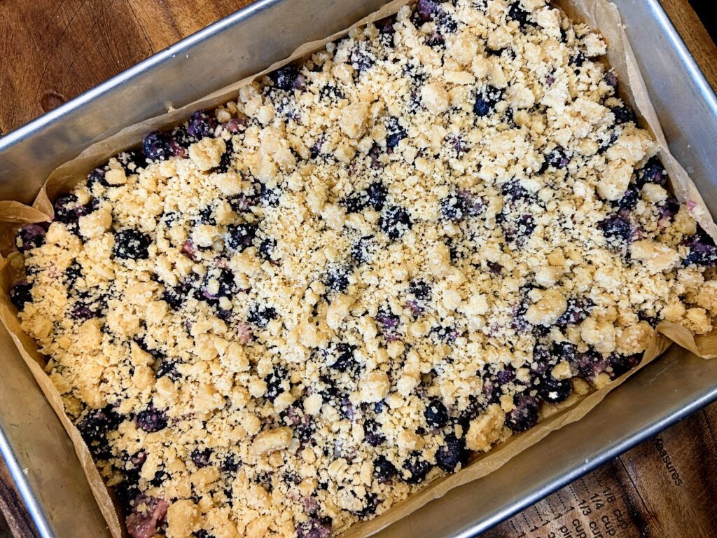 Blueberry crumble bars before baking with crumb topping sprinkled over the berry filling.