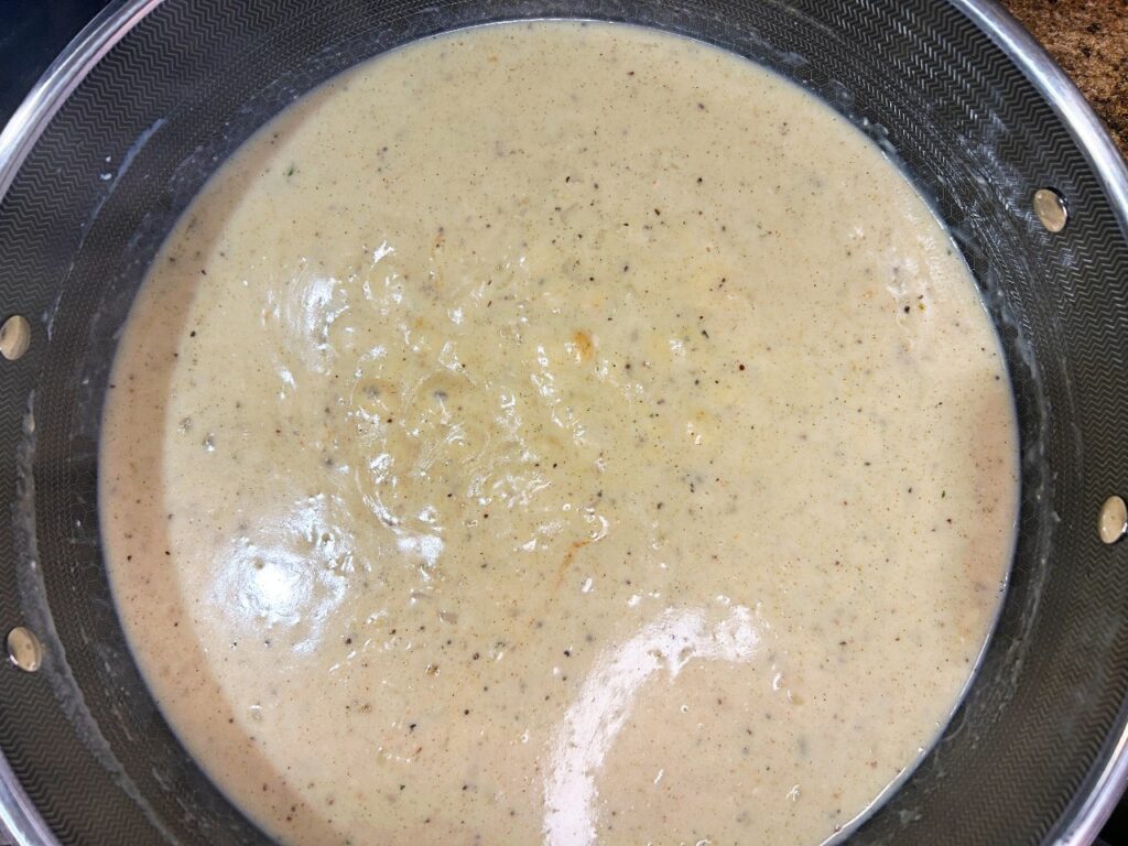 Homemade garlic herb cream sauce simmering in a skillet getting thicker