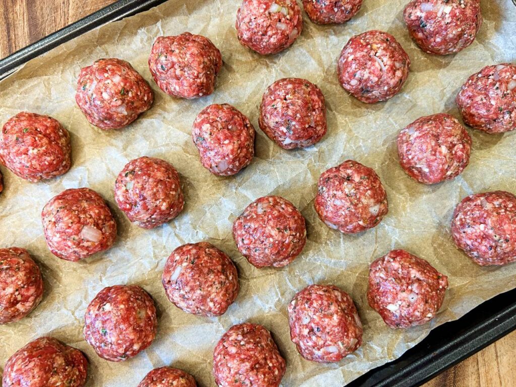 Beef meatballs rolled and ready to bake on a sheet pan.
