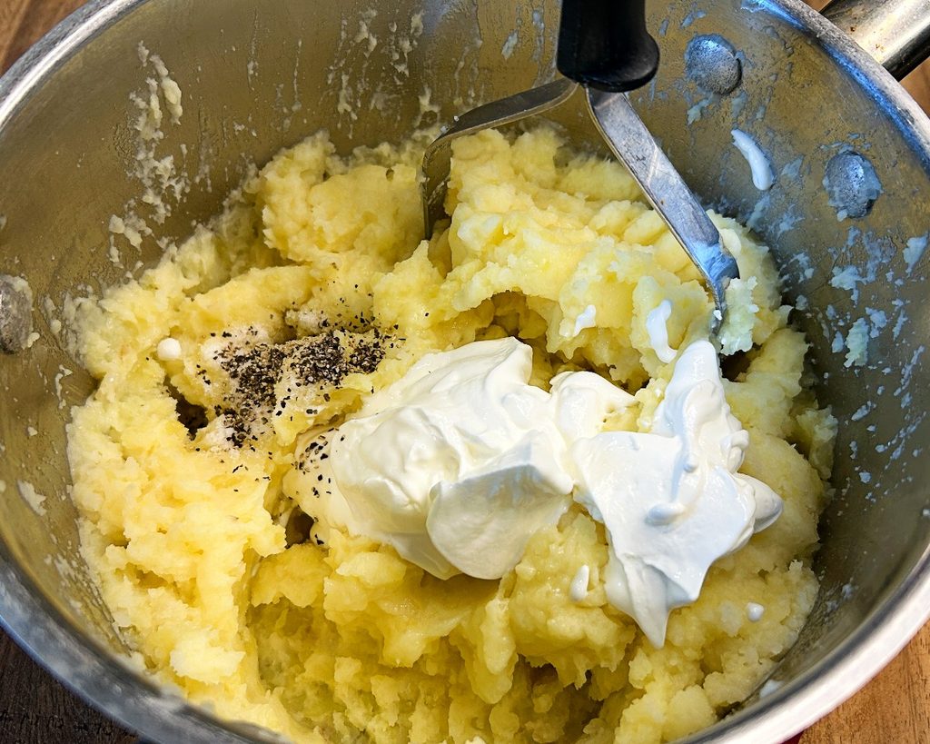 Sour cream being added to homemade mashed potatoes