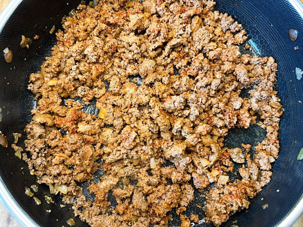 browned ground beef in a skillet with onion and garlic