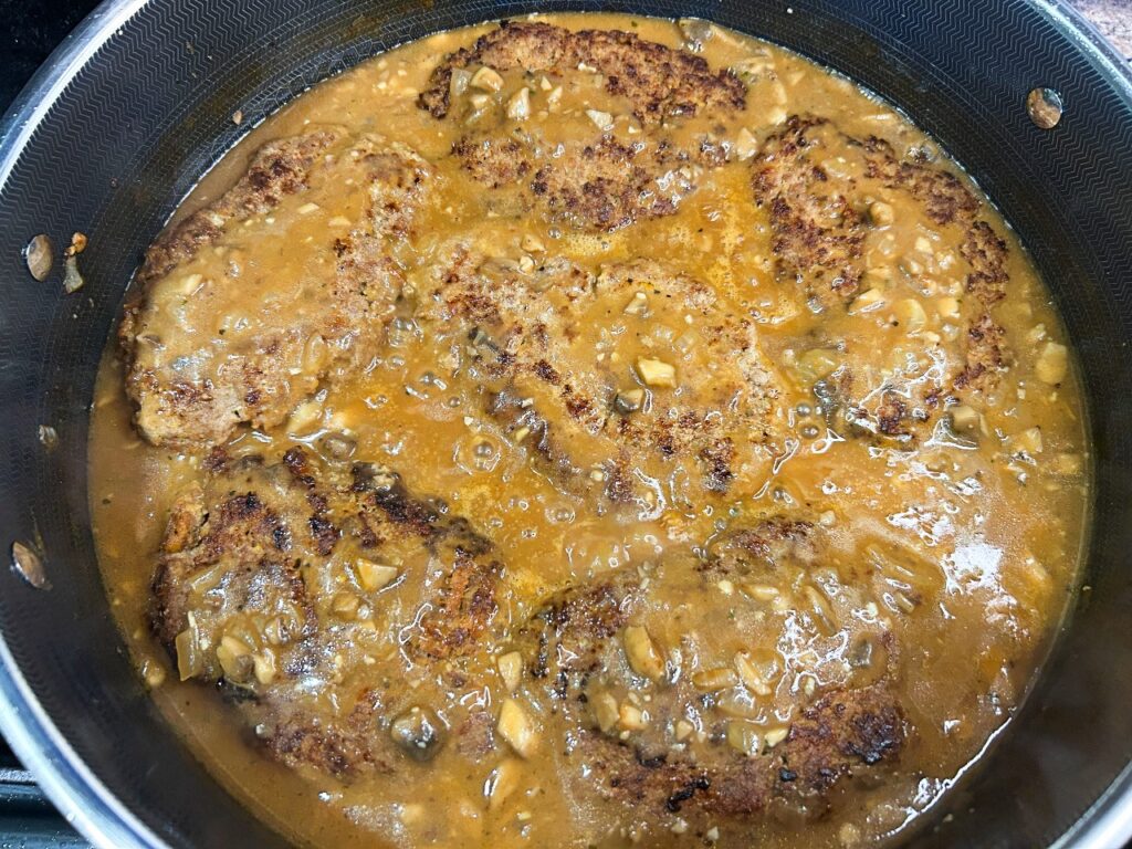Salisbury steak gravy simmering in skillet with beef patties