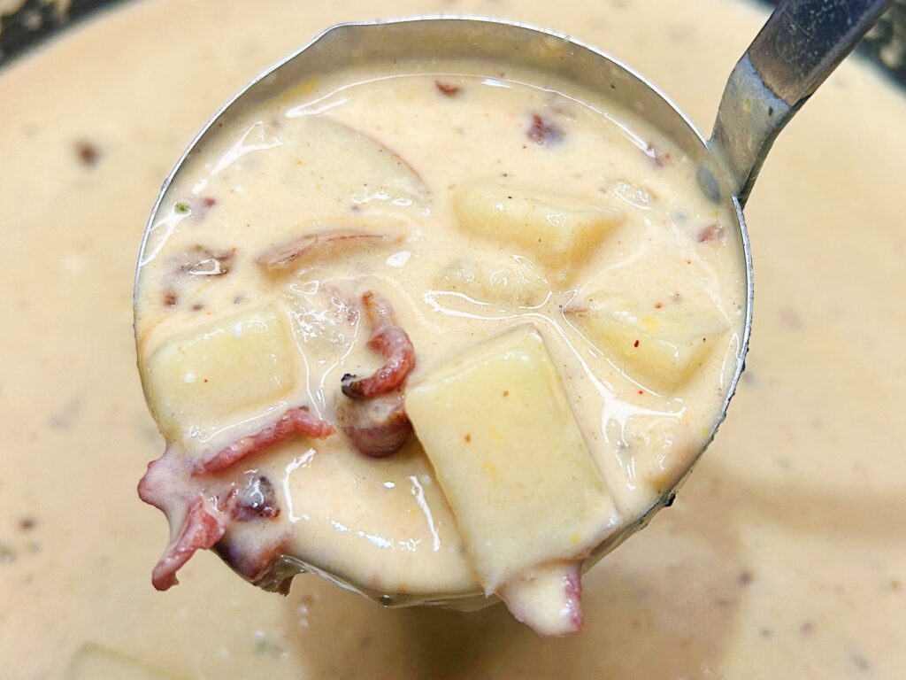 a ladle of creamy loaded potato soup showing tender potato chunks and bacon