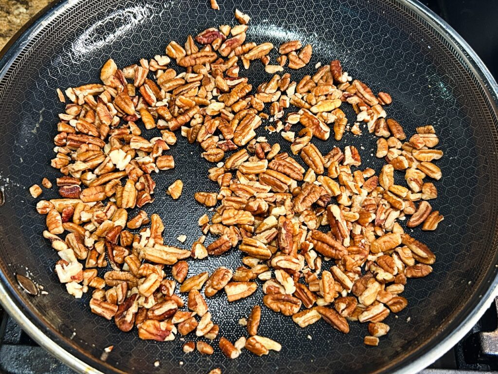 Chopped pecans toasting in a skillet for maple pecan oatmeal cookies.